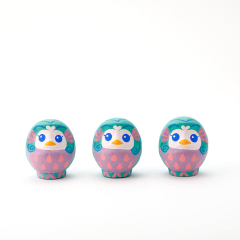 Three Imai Daruma Naya Amabie-sama, lucky creature papier-mache Japanese dolls. Each one has a purple stomach with pink scales, a turquoise head and white face, featuring blue eyes and yellow beak.