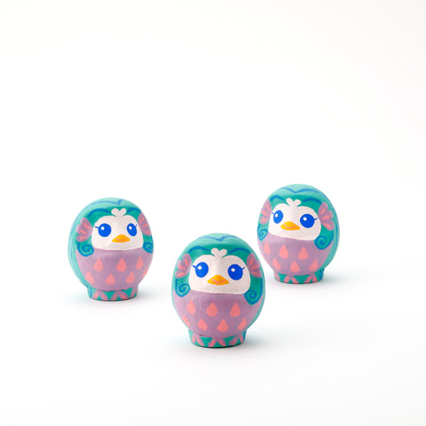 Three Imai Daruma Naya Amabie-sama, lucky creature papier-mache Japanese dolls. Each one has a purple stomach with pink scales, a turquoise head and white face, featuring blue eyes and yellow beak.