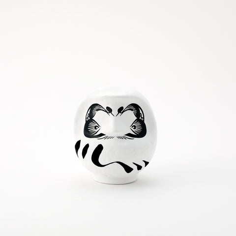 A small white Imai Daruma Naya Designer’s Daruma Japanese papier-mache doll, featuring a pattern of white eyebrows and beard and a three swirl lines across its body.