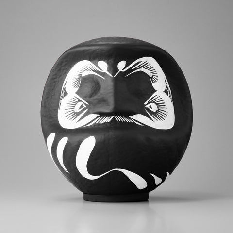 A large black Imai Daruma Naya Designer’s Daruma Japanese papier-mache doll, featuring a pattern of white eyebrows and beard and a three swirl lines across its body.