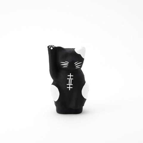 A black Imai Daruma Naya Designer Neko cat Japanese manekineko papier-mache doll, featuring white patches and whiskers and raising its right paw to beckon good luck.