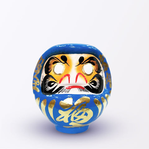 A 17-centimeter tall blue Fuku-iri lucky daruma doll, made by Imai Daruma Naya, featuring a rotund body and decorative patterns for eyebrows and beard and gold body lines and kanji lettering.