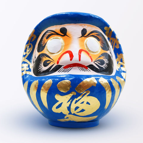 A 23-centimeter tall blue Fuku-iri lucky daruma doll, made by Imai Daruma Naya, featuring a rotund body and decorative patterns for eyebrows and beard and gold body lines and kanji lettering.