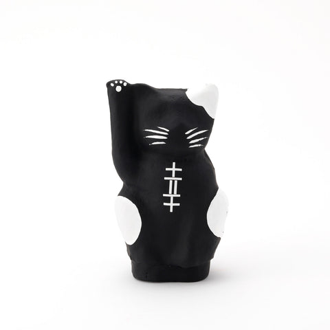 A black Imai Daruma Naya Designer Neko cat Japanese manekineko papier-mache doll, featuring white patches and whiskers and raising its right paw to beckon good luck.