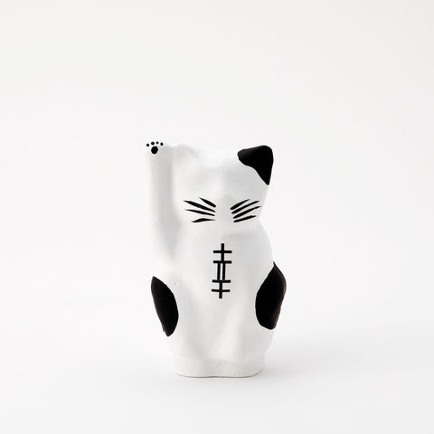 A white Imai Daruma Naya Designer Neko cat Japanese manekineko papier-mache doll, featuring black patches and whiskers and raising its right paw to beckon good luck.