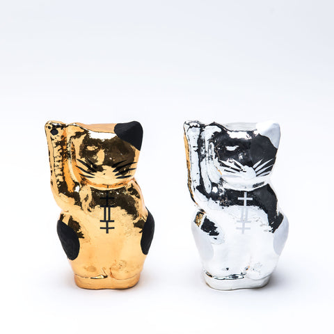 A pair of Imai Daruma Naya Platinum Designer Neko cat Japanese manekineko papier-mache dolls — one gold and one silver — both raising their right paws to beckon good luck. The gold features black patches and whiskers, the silver has white patches and whiskers.