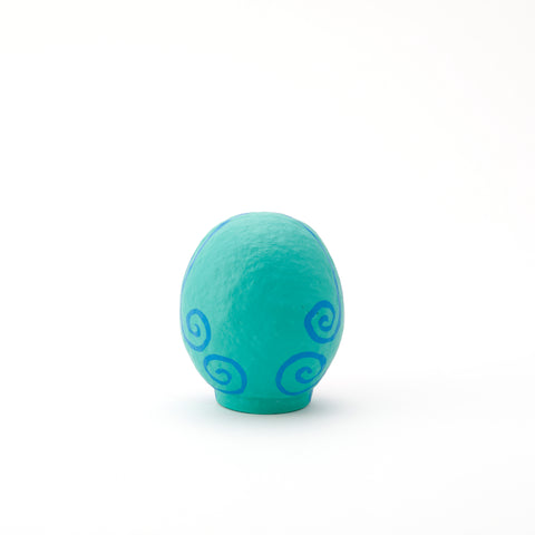 A rear view of an Imai Daruma Naya Amabie-sama, lucky creature papier-mache Japanese doll, showing its turquoise back with a blue swirl pattern.