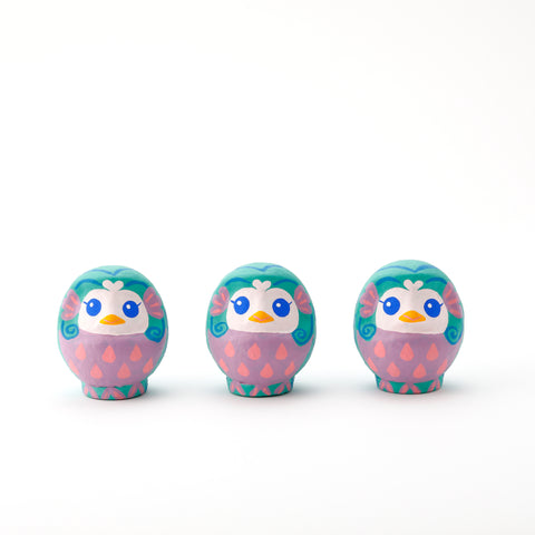 Three Imai Daruma Naya Amabie-sama, lucky creature papier-mache Japanese dolls. Each one has a purple stomach with pink scales, a turquoise head and white face, featuring blue eyes and yellow beak. 