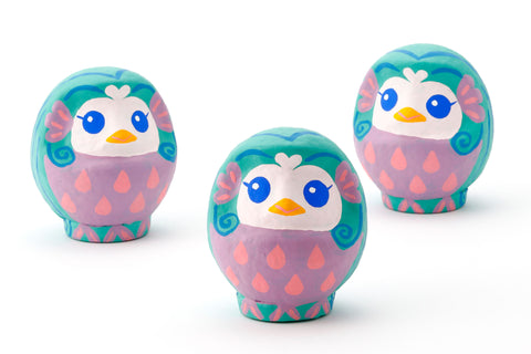 Three Imai Daruma Naya Amabie-sama, lucky creature papier-mache Japanese dolls. Each one has a purple stomach with pink scales, a turquoise head and white face, featuring blue eyes and yellow beak. 