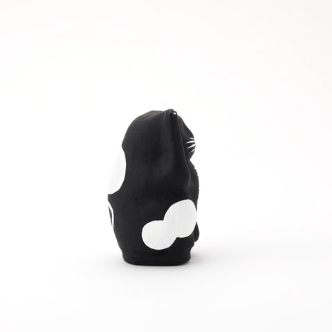 A side view of a black Imai Daruma Naya Designer Neko cat Japanese manekineko papier-mache doll, featuring white patches and whiskers and raising its right paw to beckon good luck.