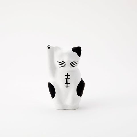 A white Imai Daruma Naya Designer Neko cat Japanese manekineko papier-mache doll, featuring black patches and whiskers and raising its right paw to beckon good luck.