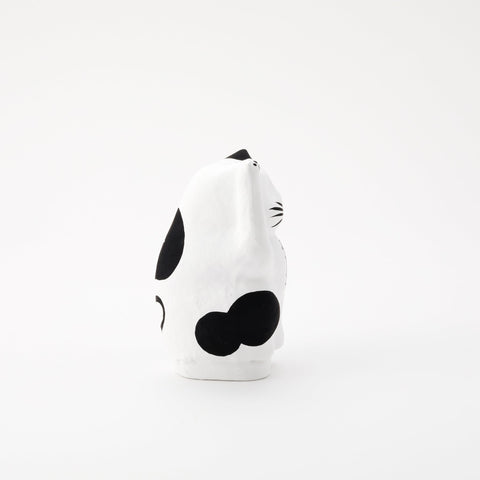  A side view of a white Imai Daruma Naya Designer Neko cat Japanese manekineko papier-mache doll, featuring black patches and whiskers and raising its right paw to beckon good luck.