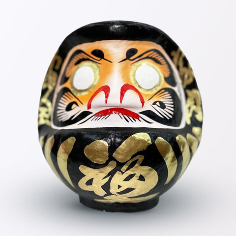A 23-centimeter tall black Fuku-iri lucky daruma doll, made by Imai Daruma Naya, featuring a rotund body and decorative patterns for eyebrows and beard and gold body lines and kanji lettering.
