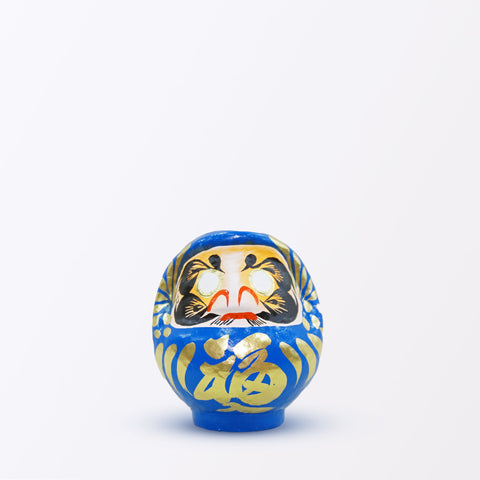 A 12-centimeter tall blue Fuku-iri lucky daruma doll, made by Imai Daruma Naya, featuring a rotund body and decorative patterns for eyebrows and beard and gold body lines and kanji lettering.