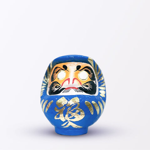 A 15-centimeter tall blue Fuku-iri lucky daruma doll, made by Imai Daruma Naya, featuring a rotund body and decorative patterns for eyebrows and beard and gold body lines and kanji lettering.