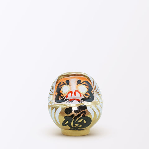 A 12-centimeter tall gold Fuku-iri lucky daruma doll, mmade by Imai Daruma Naya, featuring a rotund body and decorative patterns for eyebrows and beard and white body lines with black kanji lettering.