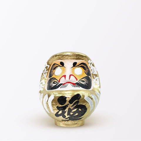 A 15-centimeter tall gold Fuku-iri lucky daruma doll, made by Imai Daruma Naya, featuring a rotund body and decorative patterns for eyebrows and beard and gold body lines and kanji lettering.