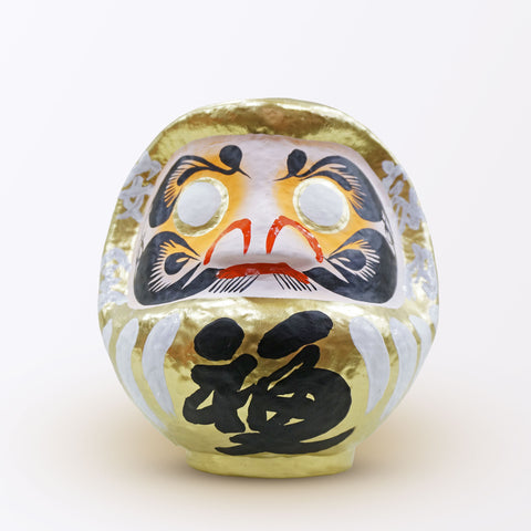 A 20-centimeter tall gold Fuku-iri lucky daruma doll, made by Imai Daruma Naya, featuring a rotund body and decorative patterns for eyebrows and beard and white body lines with black kanji lettering.