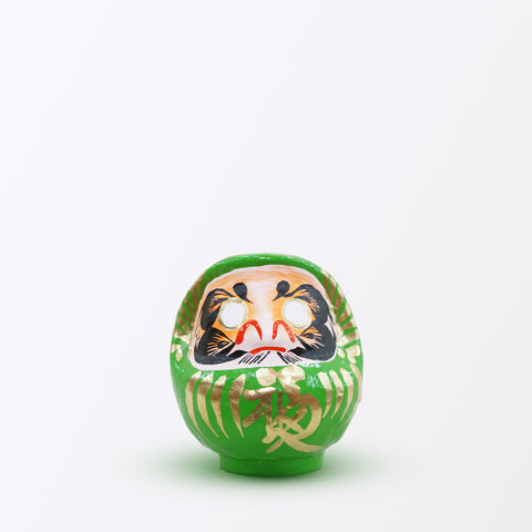 A 12-centimeter tall green Fuku-iri lucky daruma doll, made by Imai Daruma Naya, featuring a rotund body and decorative patterns for eyebrows and beard and gold body lines and kanji lettering.