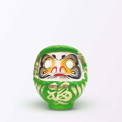 A 15-centimeter tall green Fuku-iri lucky daruma doll, made by Imai Daruma Naya, featuring a rotund body and decorative patterns for eyebrows and beard and gold body lines and kanji lettering.