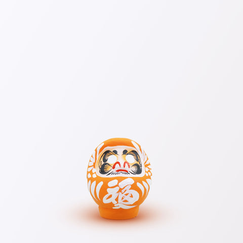 A 9-centimeter tall orange Fuku-iri lucky daruma doll, made by Imai Daruma Naya, featuring a rotund body and decorative patterns for eyebrows and beard and white body lines and kanji lettering.