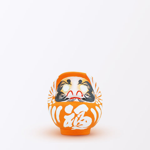 A 12-centimeter tall orange Fuku-iri lucky daruma doll, made by Imai Daruma Naya, featuring a rotund body and decorative patterns for eyebrows and beard and white body lines and kanji lettering.