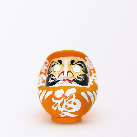 A 15-centimeter tall orange Fuku-iri lucky daruma doll, made by Imai Daruma Naya, featuring a rotund body and decorative patterns for eyebrows and beard and white body lines and kanji lettering.