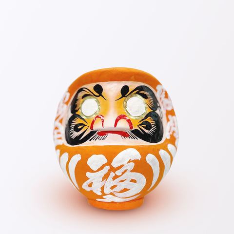 A 17-centimeter tall orange Fuku-iri lucky daruma doll, made by Imai Daruma Naya, featuring a rotund body and decorative patterns for eyebrows and beard and white body lines and kanji lettering.