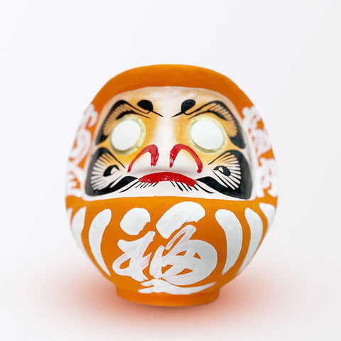 A 20-centimeter tall orange Fuku-iri lucky daruma doll, made by Imai Daruma Naya, featuring a rotund body and decorative patterns for eyebrows and beard and white body lines and kanji lettering.