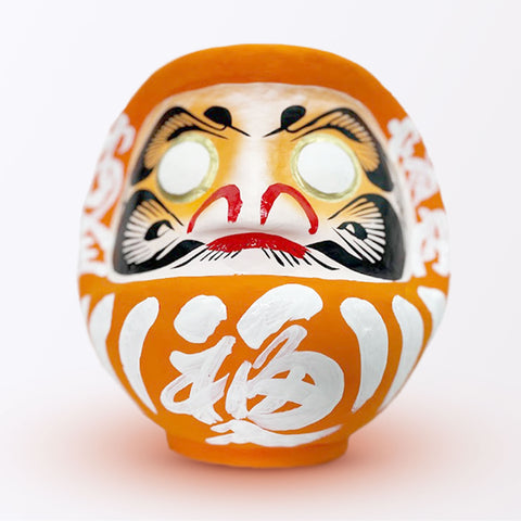 A 23-centimeter tall orange Fuku-iri lucky daruma doll, made by Imai Daruma Naya, featuring a rotund body and decorative patterns for eyebrows and beard and white body lines and kanji lettering.