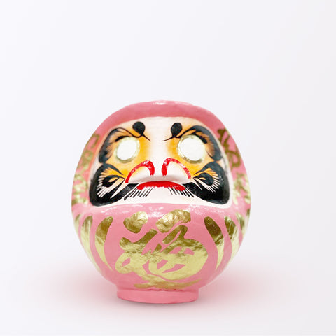 A 17-centimeter tall peach pink Fuku-iri lucky daruma doll, made by Imai Daruma Naya, featuring a rotund body and decorative patterns for eyebrows and beard and gold body lines and kanji lettering.