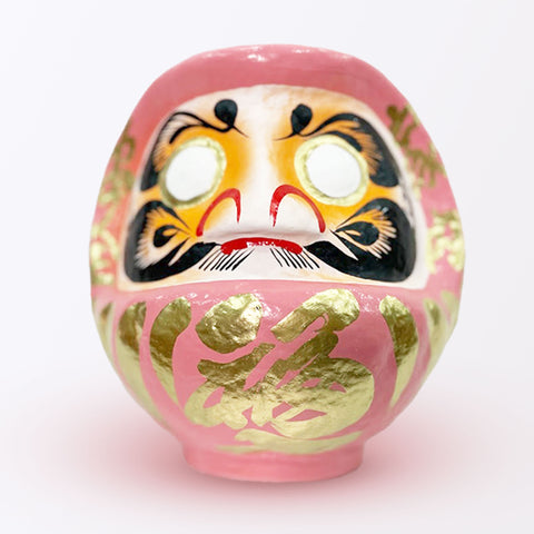 A 23-centimeter tall peach pink Fuku-iri lucky daruma doll, made by Imai Daruma Naya, featuring a rotund body and decorative patterns for eyebrows and beard and gold body lines and kanji lettering.