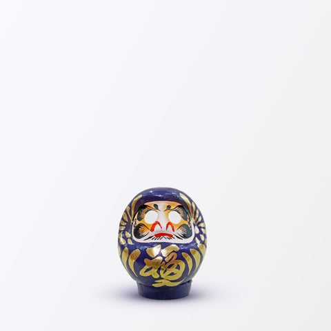 A 9-centimeter tall purple Fuku-iri lucky daruma doll, made by Imai Daruma Naya, featuring a rotund body and decorative patterns for eyebrows and beard and gold body lines and kanji lettering.