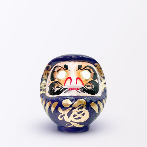 A 15-centimeter tall purple Fuku-iri lucky daruma doll, made by Imai Daruma Naya, featuring a rotund body and decorative patterns for eyebrows and beard and gold body lines and kanji lettering.