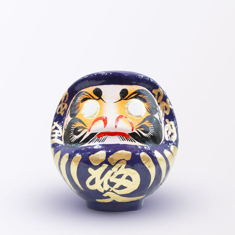 A 17-centimeter tall purple Fuku-iri lucky daruma doll, made by Imai Daruma Naya, featuring a rotund body and decorative patterns for eyebrows and beard and gold body lines and kanji lettering.