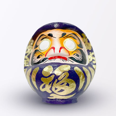 A 20-centimeter tall purple Fuku-iri lucky daruma doll, made by Imai Daruma Naya, featuring a rotund body and decorative patterns for eyebrows and beard and gold body lines and kanji lettering.