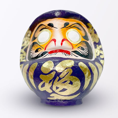 A 23-centimeter tall purple Fuku-iri lucky daruma doll, made by Imai Daruma Naya, featuring a rotund body and decorative patterns for eyebrows and beard and gold body lines and kanji lettering.