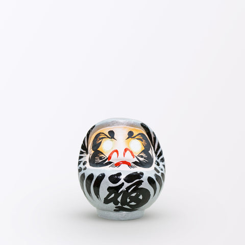 A 12-centimeter tall silver Fuku-iri papier-mache daruma dolls, made by Imai Daruma Naya. All feature rotund bodies, decorative patterns for eyebrows and beards and black body lines and kanji lettering.