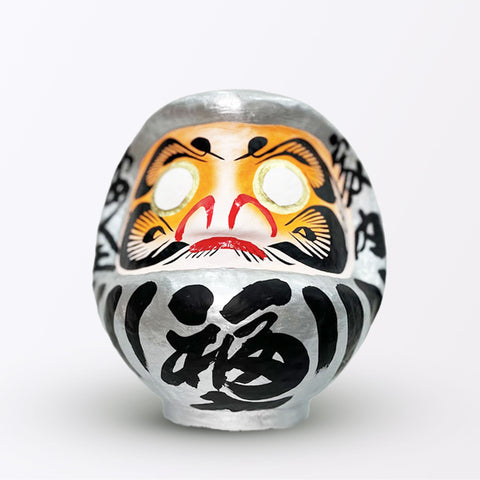 A 20-centimeter tall silver Fuku-iri papier-mache daruma dolls, made by Imai Daruma Naya. All feature rotund bodies, decorative patterns for eyebrows and beards and black body lines and kanji lettering.