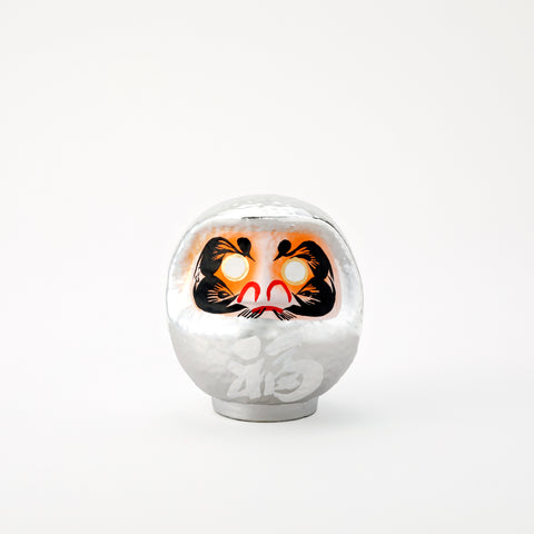 A shiny, silver Platinum Daruma lucky doll, made by Imai Daruma Naya. The rotund doll features decorative patterns for its eyebrows and beard, and white kanji lettering.