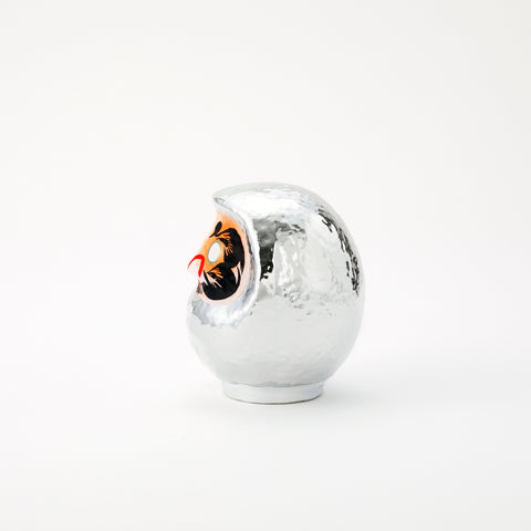 A side view of a shiny, silver Platinum Daruma lucky doll, made by Imai Daruma Naya. The rotund doll features decorative patterns for its eyebrows and beard, and white kanji lettering.